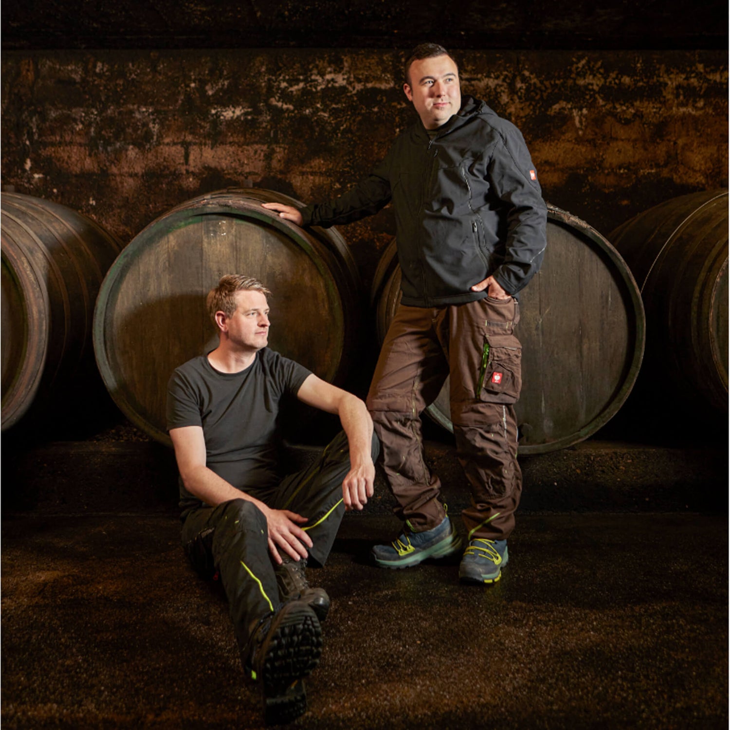 Corvin Prigge und Florian Maring vor Holzfuderfässern sitzen / stehend im Weinkeller